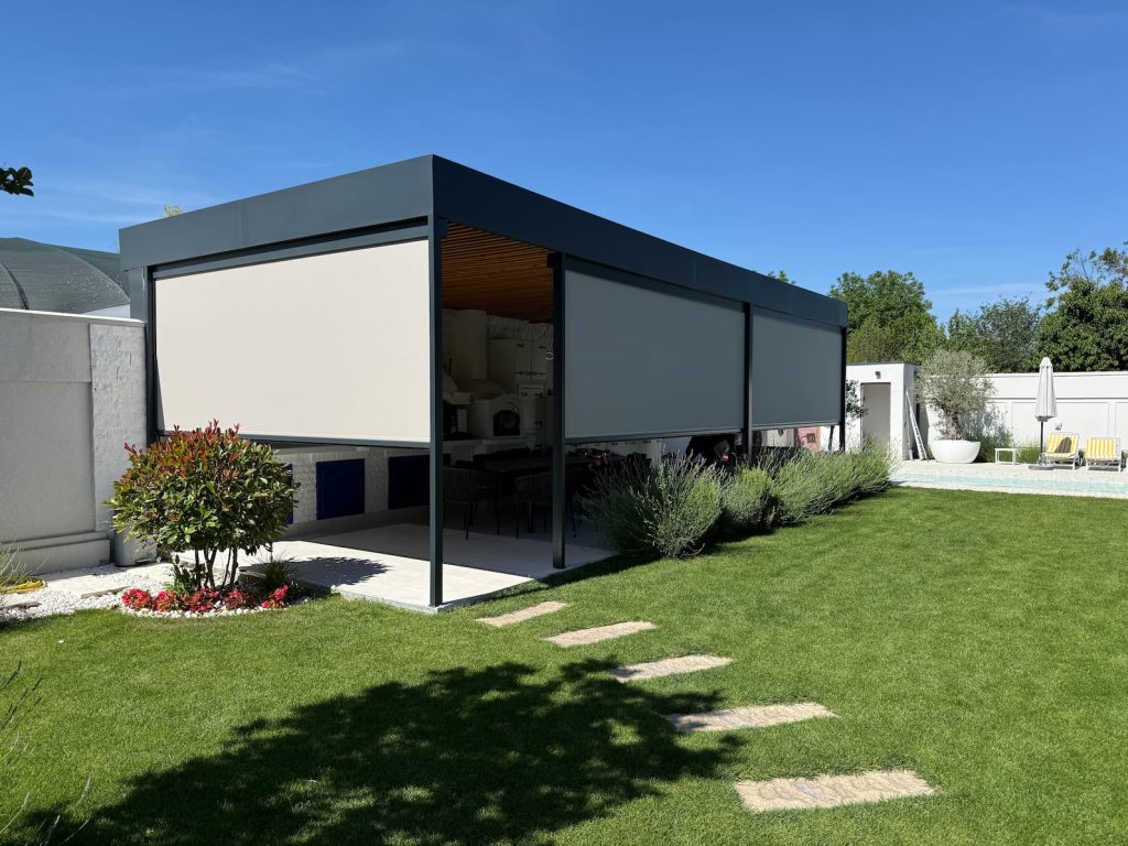 Moderna antracit pergola sa spuštenim ZIP sistemima u boji peska, okružena travnjakom, lavandom i bazenom